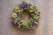 Handmade wreath of purple and yellow flowers for your home door decoration isolated on a gray concrete background.