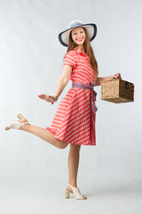 Young cheerful woman in red dress posing with picnic basket in studio on white background