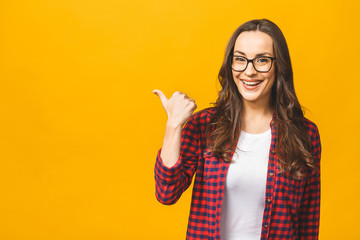 Image of happy young lady standing isolated over yellow background. Looking camera pointing. Thumbs up.