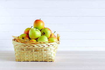 Basket with apples on wooden white table, insulation on white background.