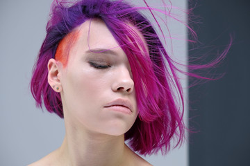 Concept Portrait of a punk girl, young woman with chic purple hair color in studio close up on a colorful background with fluttering hair.