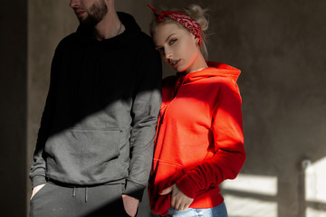 Beautiful young stylish couple in trendy hoodie indoors with sunshine. Hipster girl in red hoodie and handsome man with beard in blue hoodie in studio