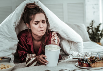 Wall Mural - Stressed woman covered with a blanket eating sweets