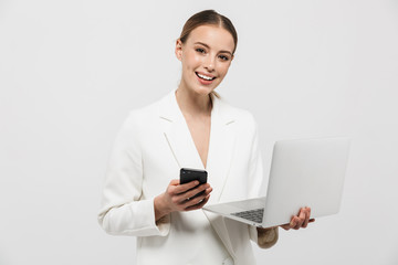 Photo of pretty businesswoman 20s wearing elegant jacket smiling while holding laptop and smartphone