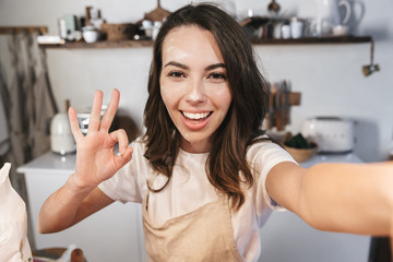 Cheerful young girl covered with flour taking a selfie