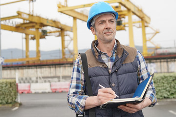 Mature construction worker inspecting work sight with notebook