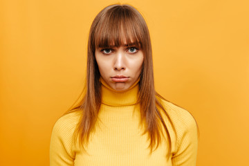 Woman portrait. Emotion. Beautiful young woman is pouting her lips at camera, on a yellow background