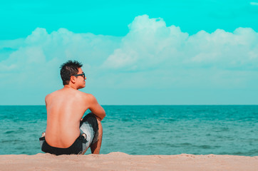 Man seated on the sand of the beach staring the sea. Cyan and orange tones. Photo at Praia de Tabatinga 2, Conde PB Brazil. 