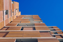 View From The Floor Of The Facade Of A Modern Building Clad In Ecological Wood Over Clean Blue Sky, Concept Of Sustainable Construction Background, Copy Space.