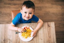 A Child In A T-shirt In The Kitchen Eating An Omelet, A Fork