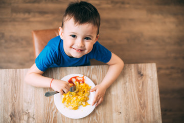 a child in a t-shirt in the kitchen eating an omelet, a fork