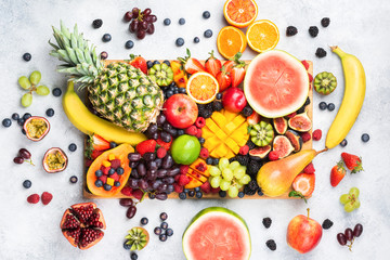 Wall Mural - Healthy raw rainbow fruit platter background, mango papaya strawberries oranges blueberries pineapple watermelon on wooden board on light concrete background, top view, selective focus