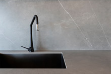 A Black Sink And A Matt-finish Black Faucet Set Against Grey Surfaces Made Of Porcelain Slabs That Mimic The Look Of Natural Stones