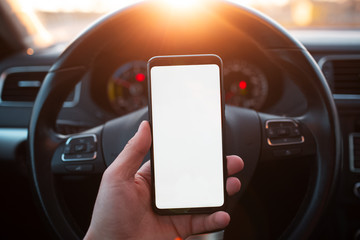 Handing a smartphone with mockup in the car on sunset background.