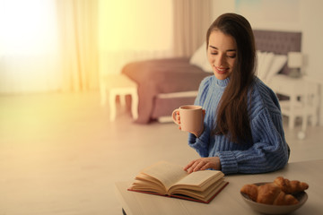 Sticker - Young woman drinking coffee and reading book at table indoors, space for text