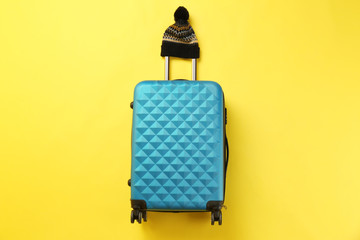 Stylish suitcase with warm hat on color background, top view