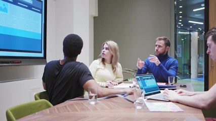 Wall Mural - Tracking shot of diverse business team with experienced manager discussing website templates presented on interactive digital board and examining printed marketing research