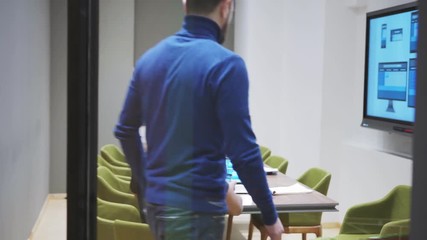 Wall Mural - Manager walking along corridor and entering office where young web designer presenting him website template on laptop, digital board and smartphone