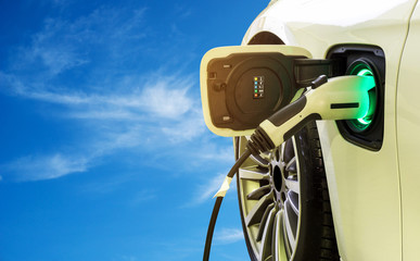 Poster - EV Car or Electric car at charging station with the power cable supply plugged in on the blue sky and cloud background. Eco-friendly alternative energy concept.