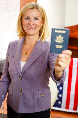 Portrait Of Smiling Senior Woman Lawyer 60 65 Years Old In Blazer Showing United State Amerika Passport To Camera In The Office Of Attorney Company With Usa Flag On Background Stock Photo