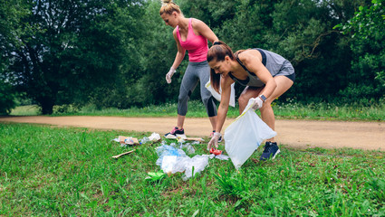 Waste pile and two girls running with bags doing plogging outdoors