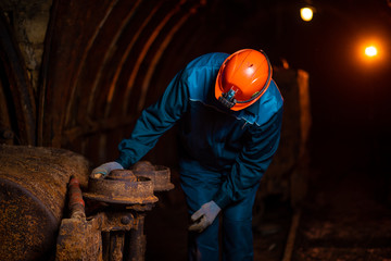 An elderly man dressed in work overalls and a helmet stands near the old inverted vogonetki. Mine worker. Miner