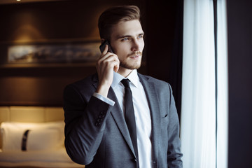 Young handsome man relaxing at his apartment in a hotel after business meeting. Business trip. Booking hotel during your vacation. Businessman in luxury room  of the expensive beautiful hotel