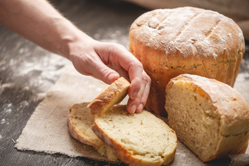 Women's hands breaking homemade natural fresh bread with a Golden crust on old wooden background. Baking bakery products