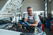 © cherryandbees - checking online for car spare parts . worker using tablet in car workshop