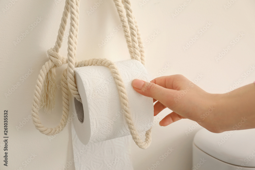 Young woman taking soft toilet paper in restroom