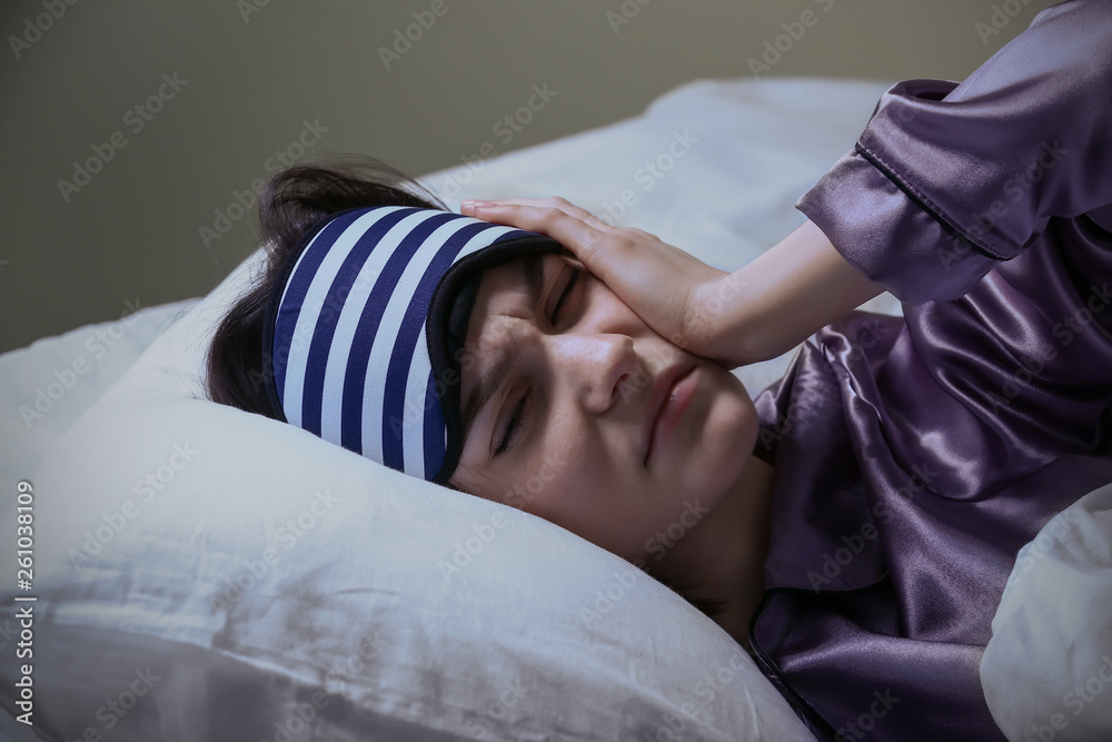Stressed woman with sleep mask in bed at night