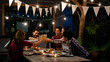 © torwaiphoto - Asian group eating and drinking cold beer outside the house at night, having fun talking