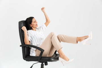 Wall Mural - Photo of happy brunette businesswoman 30s smiling and rejoicing while sitting in black armchair in office