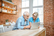 © rh2010 - Beautiful senior couple in blue shirts sitting together with laptop on the kitchen at home