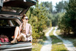 © rh2010 - Young woman enjoying nature while sitting in the car trunk on a picturesque road in the woods