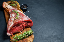 A Raw Leg Of Lamb On A Wooden Chopping Board. Rosemary, Thyme, Black Pepper. Black Background, Side View, Space For Text