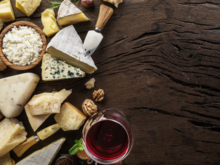 Wall Mural - Cheeses with organic cheeses, fruits, nuts and wine on old wooden background. Top view. Tasty cheese starter.
