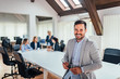 © bnenin - Handsome business man looking at camera in modern conference room. Colleagues in the background.