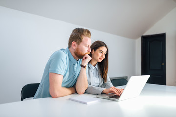 Wall Mural - Two millenial entrepreneurs looking at laptop screen in a bright meeting room.