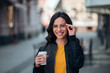 © bnenin - Portrait of smiling young woman holding paper cup, urban scene, city life.