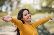 © bnenin - Close-up of happy woman standing with open arms outdoors, smiling at camera.