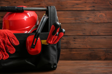 Black bag with construction tools on table against wooden background, space for text