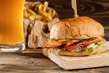 A big burger with chicken cooked on charcoal. Lunch with Glass of beer on a wooden background. The concept of fast food and unhealthy food