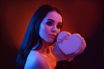 Neon red and blue light. Fashion portrait of sexy elegant beautiful brunette young woman holding heart shaped giftbox. Model with trendy evening smoky eyes makeup. Valentine's Day, Women's Day concept