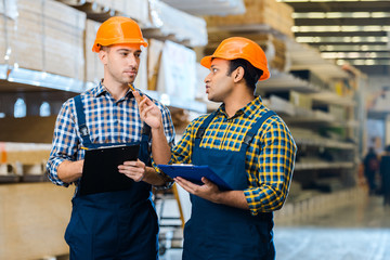 Wall Mural - two serious multicultural warehouse workers talking and holding clipboards