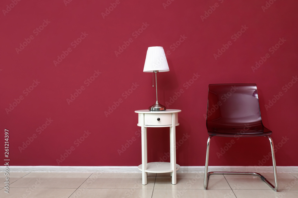 Table with lamp and chair near color wall