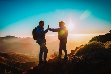 Silhouettes of father and son hiking in mountains at sunset