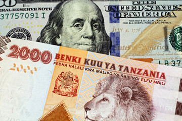 An orange and blue two thousand Tanzanian shilling bank note with a United States blue, American one hundred dollar bill in macro