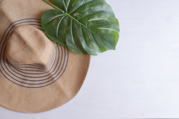 Wall Mural - Big straw hat with palm leaf on white wooden background. Summer vacation background with copy space.