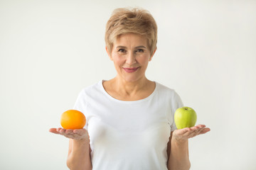 beautiful aged woman with short haircut in a white t-shirt with an apple and an orange on a white background